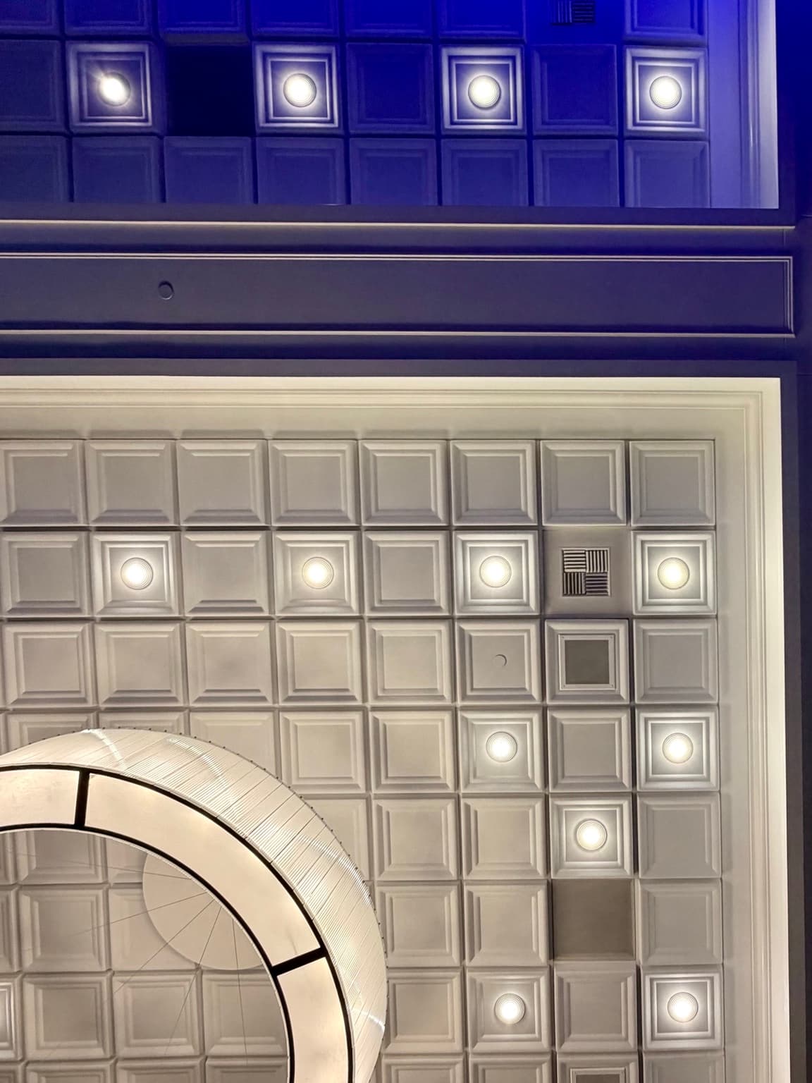 Close view of the white recessed tiles, downlights, and chandelier edge